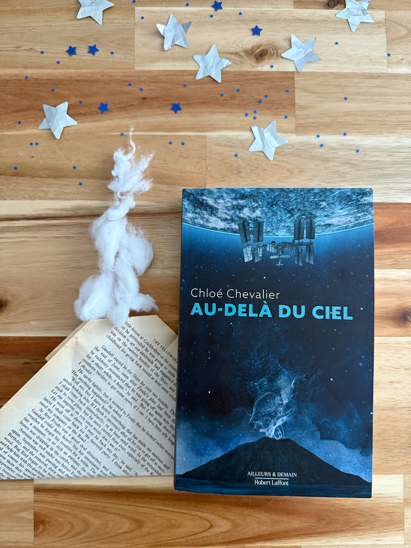 Livre Au-delà du ciel sous des étoiles en papier aux côté d’un volcan formé d’une page de roman.