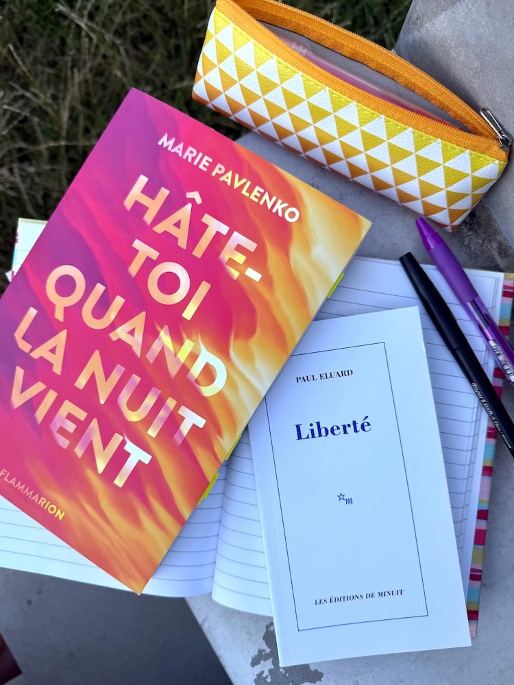 Livre Hâte-toi quand la nuit vient avec Liberté de Paul Eluard, une trousse, un cahier au-dessus d’une herbe sèche