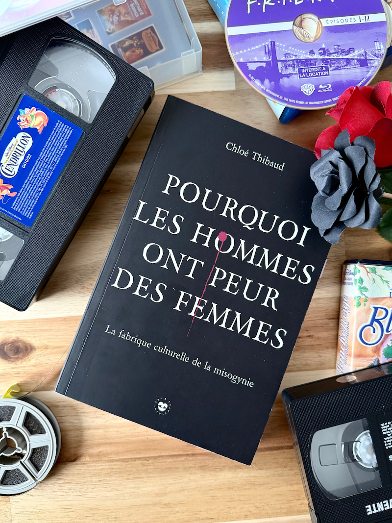 Livre Pourquoi les hommes ont peur des femmes posé aux côtés de cassettes Disney, blu-ray de Friends et Super 8 ainsi que deux fleurs rouges et noires.